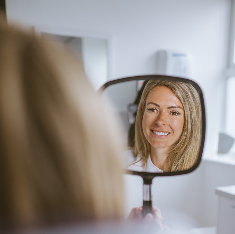 Patient viewing her brighter smile in a mirror after professional teeth-whitening treatment in Bristol