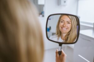 Patient looking at her improved smile in a mirror after composite bonding treatment in Bristol