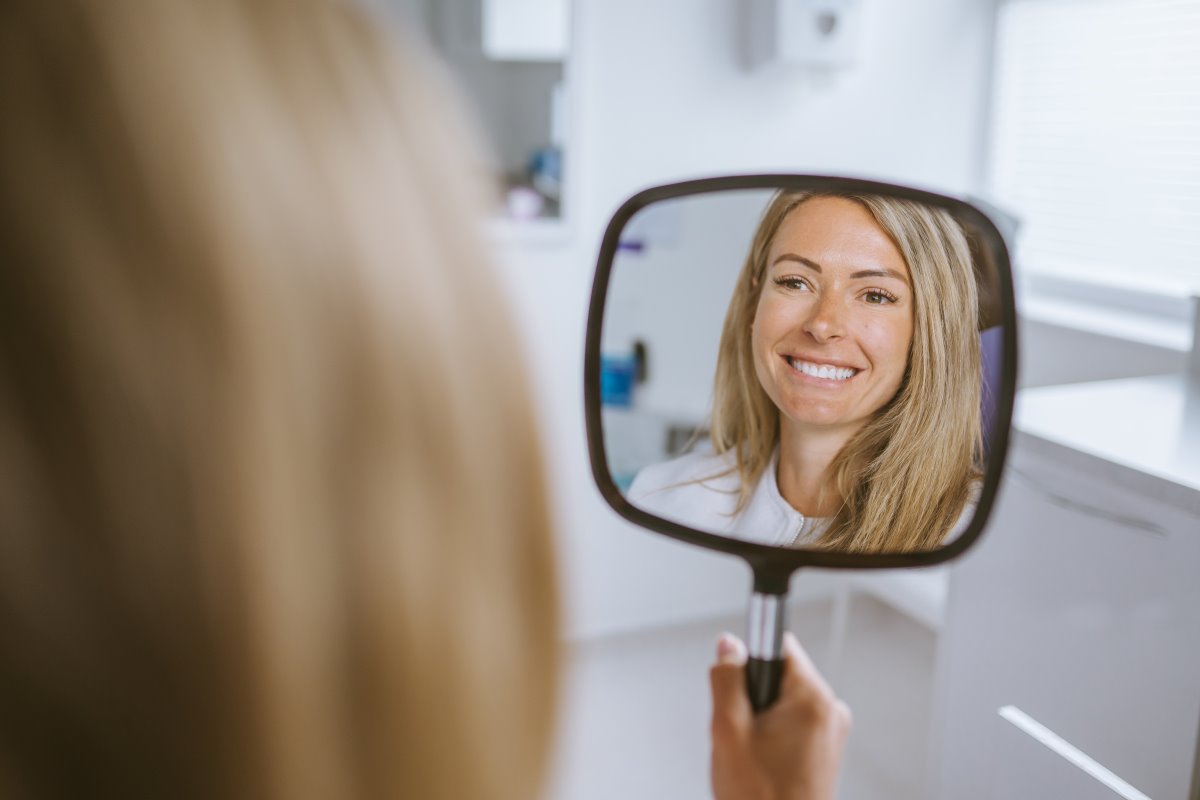 Patient looking at her improved smile in a mirror after composite bonding treatment in Bristol